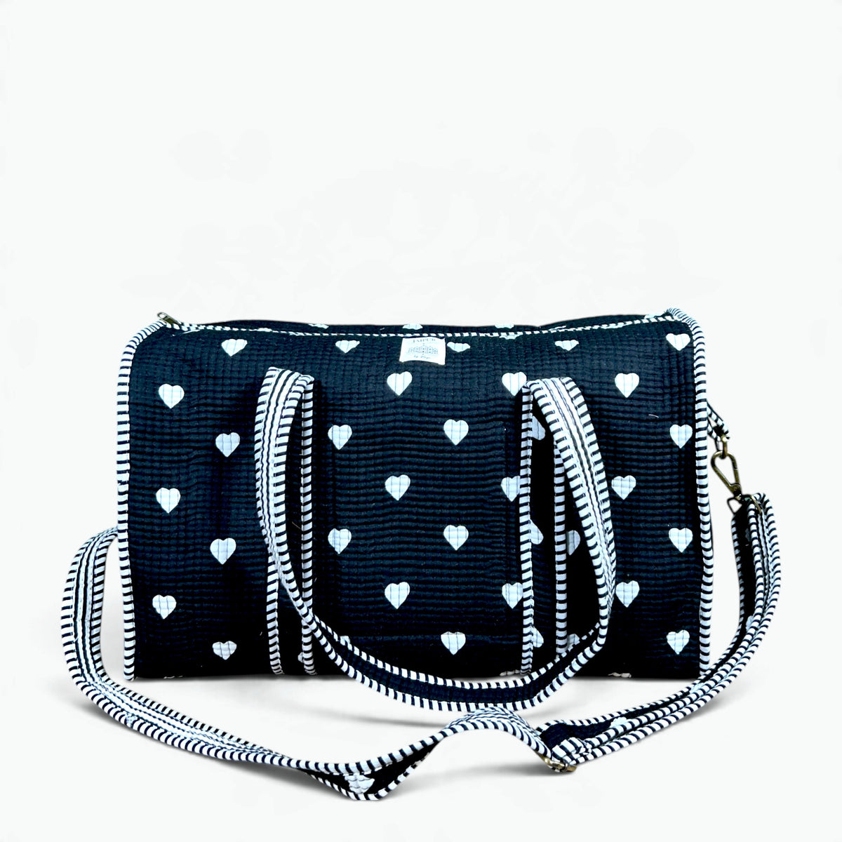 Large black quilted cotton duffle bag with white heart print, black and white striped piping, carry handles and adjustable shoulder strap