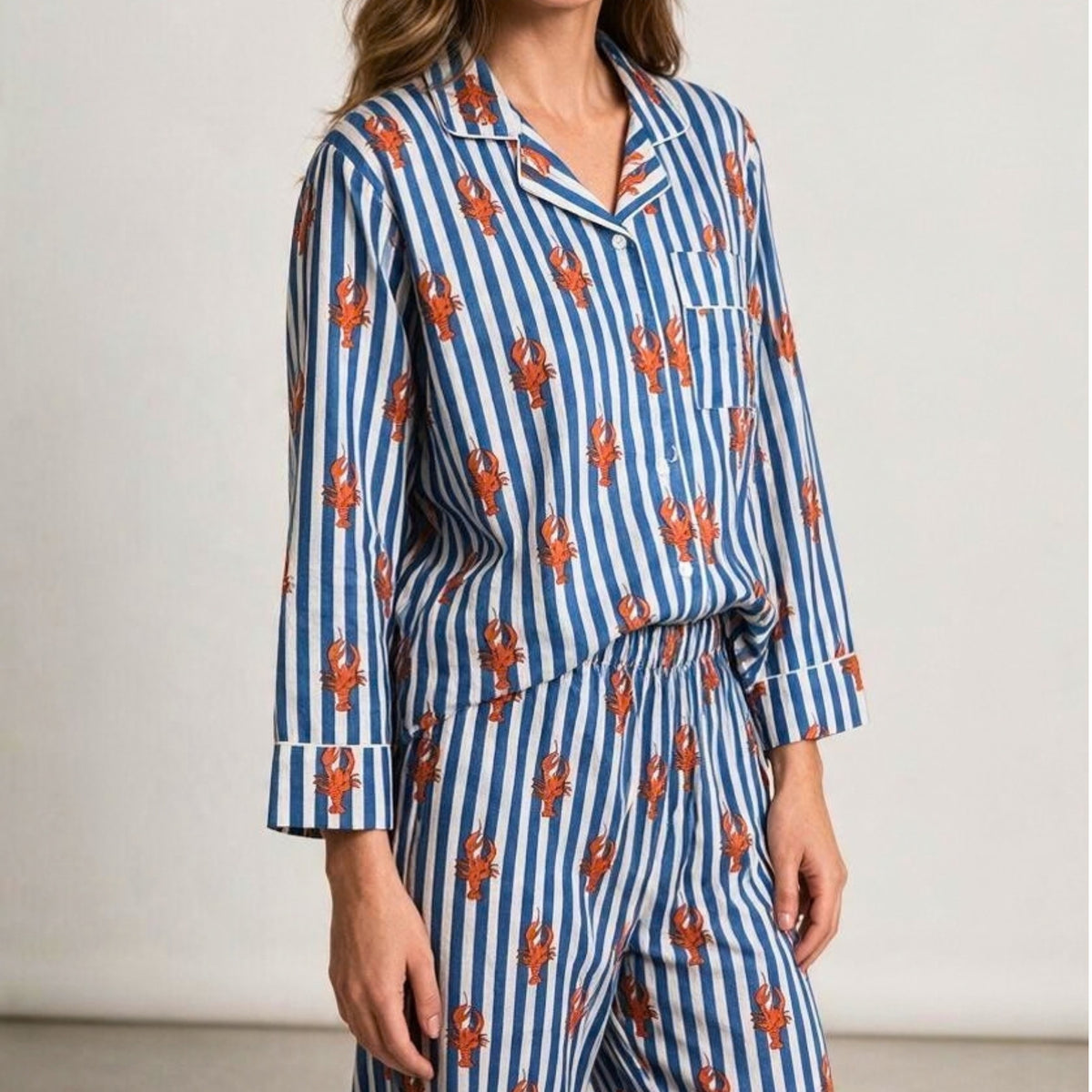 Blue and white striped cotton pyjama set featuring a red lobster print and white piping, shown with a matching fabric travel pouch.