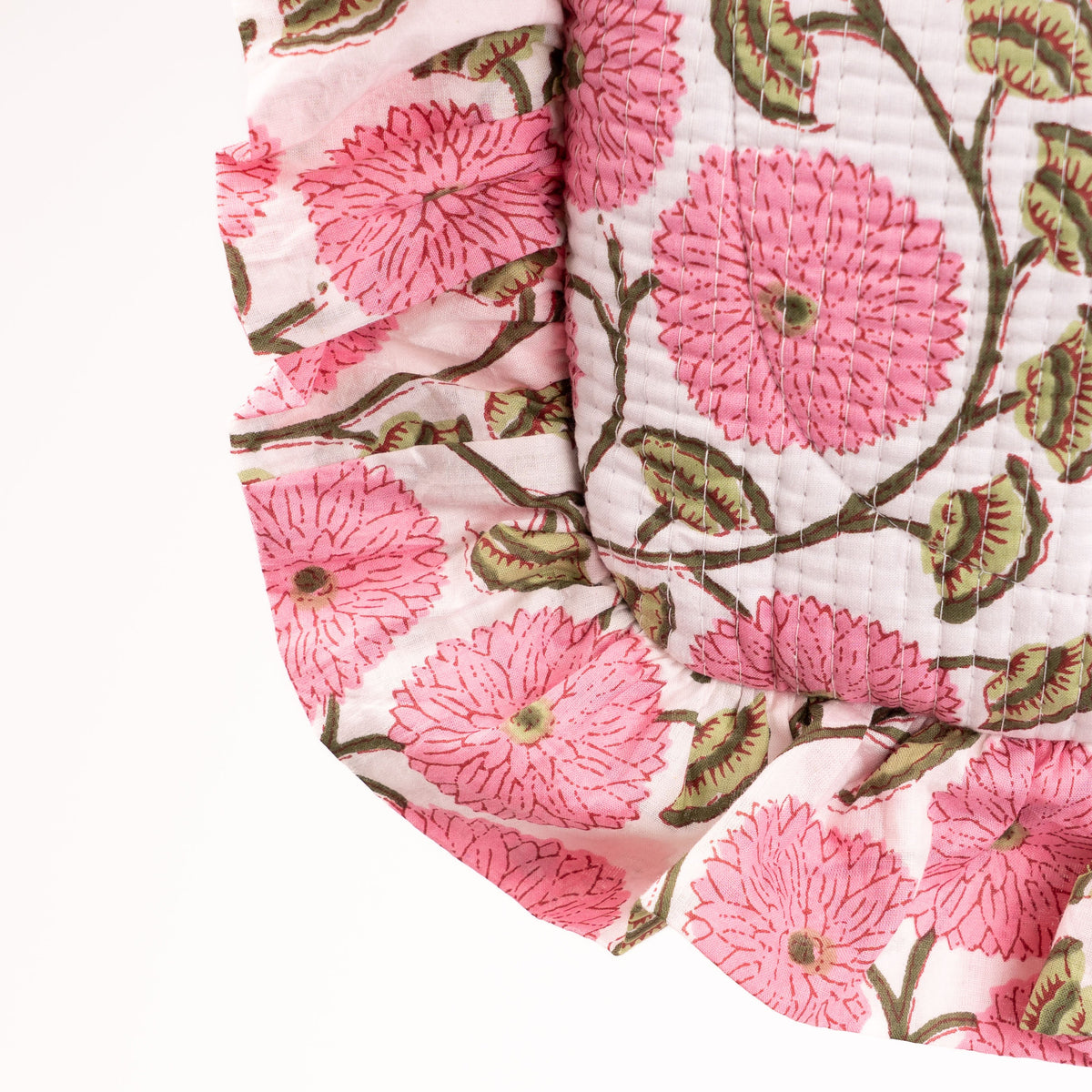A close-up of a quilted cotton blanket featuring a pink floral and green leaf pattern on a white background, with a pink and white striped fabric visible at the top edge.