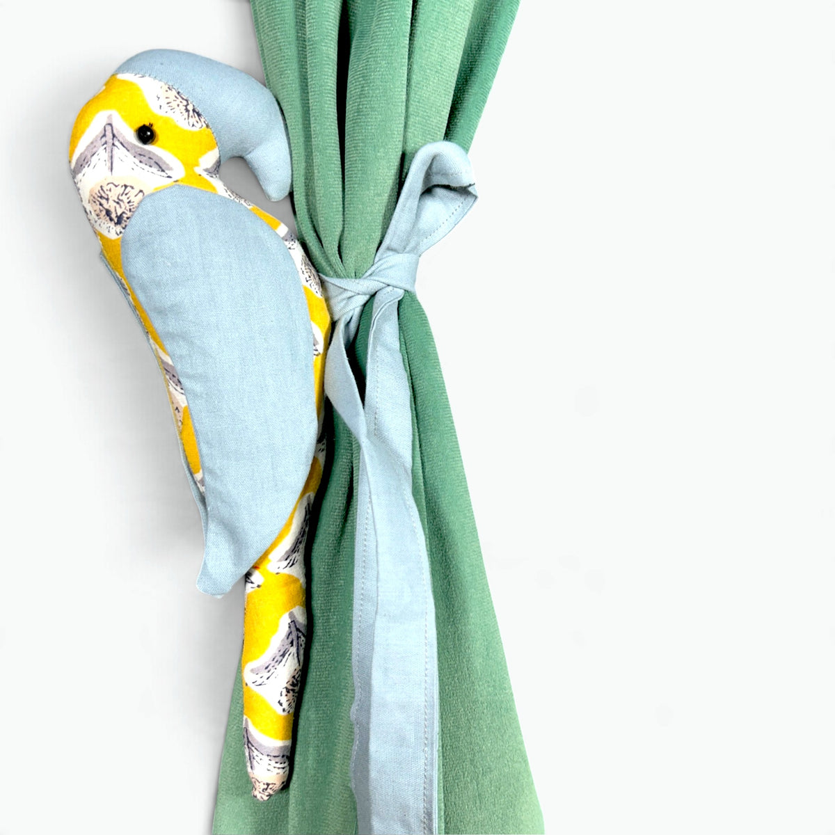 A plush bird-shaped curtain tieback or curtain panel in light blue fabric with a yellow and white patterned head, shown tied to a green curtain on a white background.