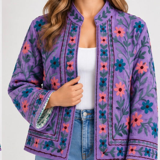 A woman wearing a purple embroidered jacket with blue and pink floral patterns, paired with a white top and light blue jeans.